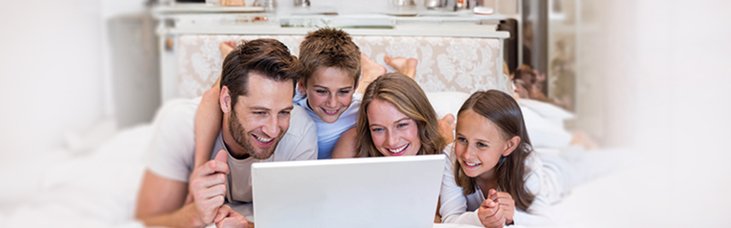 A képen egy család mosolyogva néz egy laptopot.