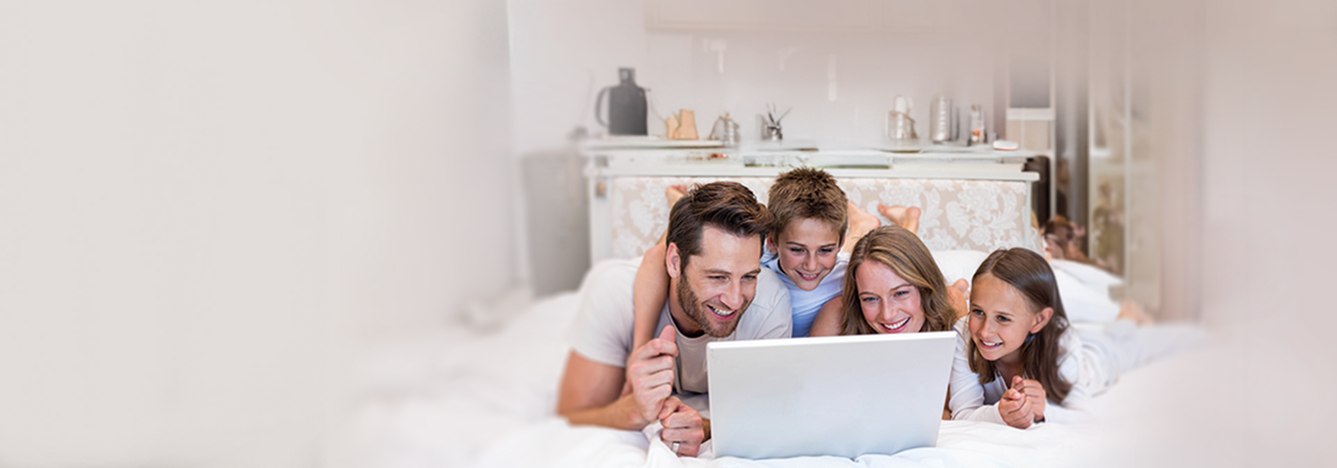A képen egy család mosolyogva néz egy laptopot.