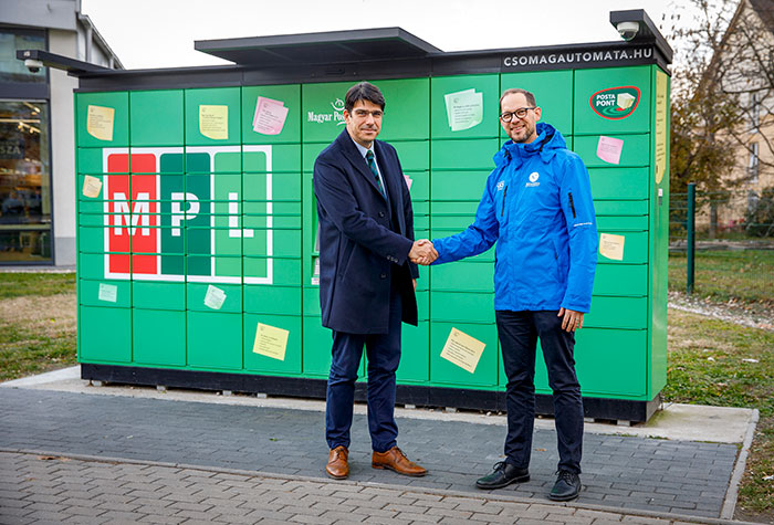 A képen dr. Mikecz Péter és Gáncs Kristóf kézfogása látható egy Magyar Posta csomagautomata előtt