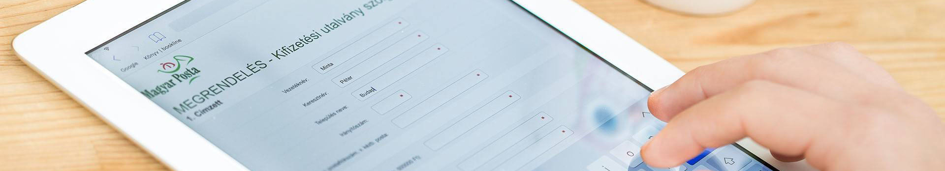 A képen egy tabletet érintő kéz látható, a kifizetés utalványi szolgáltatást ábrázoló felületen. 