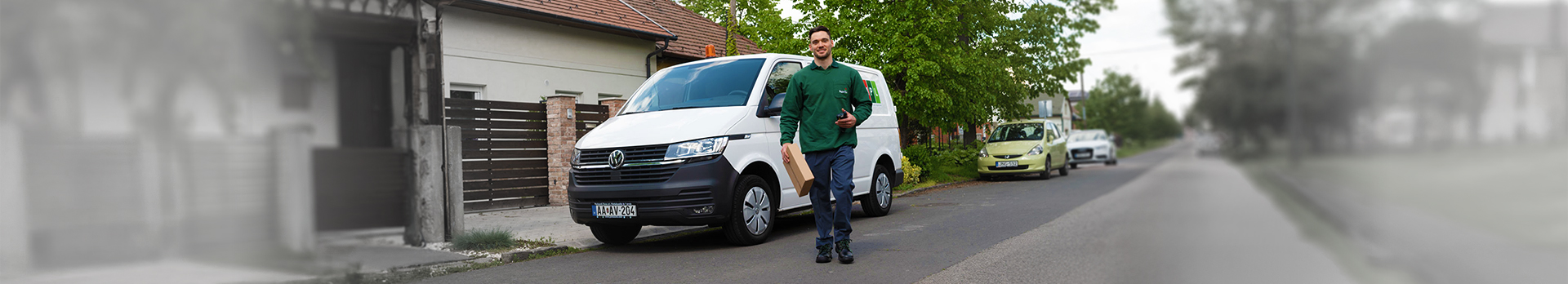 Családi házas övezetben egy mosolygós postás futár férfi látható, csomaggal a kezében, mögötte fehér MPL transzporter.