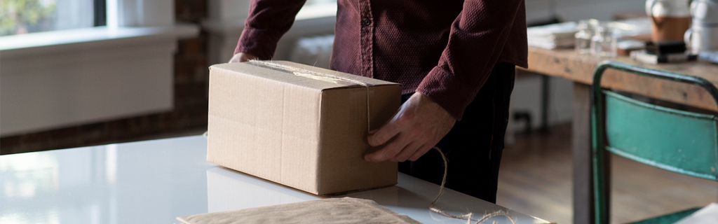 A képen egy asztal látható, rajta csomagoló papír, spárga és egy csomagoló kéz látható.