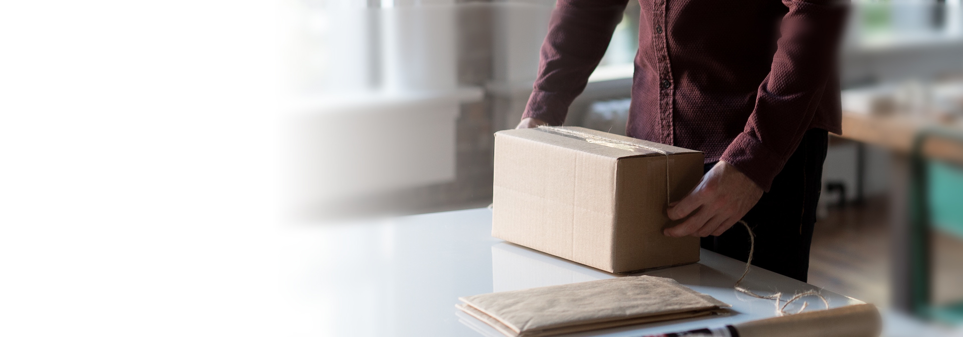 A képen egy asztal látható, rajta csomagoló papír, spárga és egy csomagoló kéz látható.