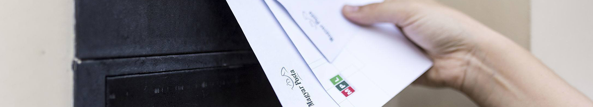 A képen egy kéz leveleket helyez a postaládába.